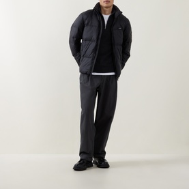 Model wearing Calvin Klein Logo Badge Padded Jacket in black, styled with dark trousers and black chunky trainers.
