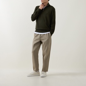 Model wearing Calvin Klein Monogram Logo Half-Zip Sweater in Olive Night, styled with beige trousers and white trainers.