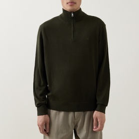 Model wearing Calvin Klein Monogram Logo Half-Zip Sweater in Olive Night, funnel neck, tonal chest logo, paired with beige trousers.