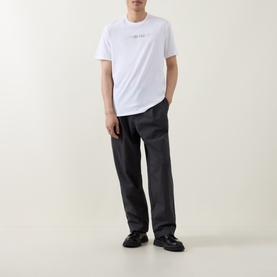 Model wearing Calvin Klein Graphic Logo T-Shirt in Bright White with dark grey trousers and black shoes.
