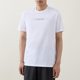 Model wearing Calvin Klein Graphic Logo T-Shirt in Bright White with crew neck and contrast logo lettering across chest, paired with black trousers.