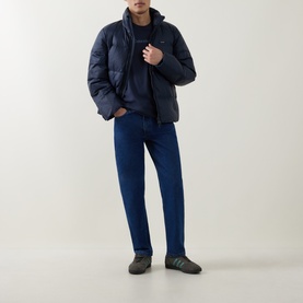 Model wearing Calvin Klein Graphic Logo T-Shirt in Blue Nights, styled with navy puffer jacket, blue jeans and grey trainers.