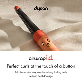 Dyson Airwrap i.d. curling barrel in coral and black with gold attachments, styled on draped fabric background