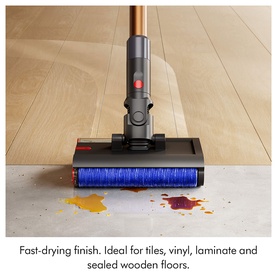 Cordless stick vacuum with blue roller head cleaning liquid spill on hard floor, shown on tile, vinyl, laminate and wood surfaces
