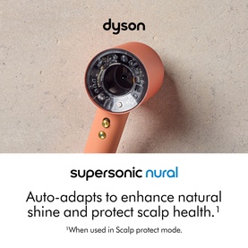 Dyson Supersonic Nural hair dryer in copper and black, nozzle-end view showing precision airflow attachment on stone surface.