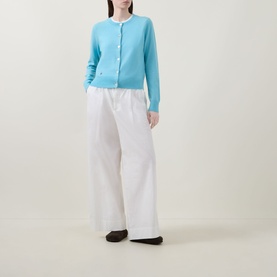 Model wearing Lucy Nagle The Everyday Cardigan in Bambino blue, fine knit with round neck and logo disc buttons, styled with wide-leg white trousers.