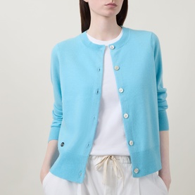 Model wearing Lucy Nagle The Everyday Cardigan in Bambino blue, round neck, logo disc buttons, fine knit, over white T-shirt with cream trousers