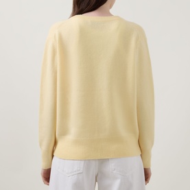 Model wearing Lucy Nagle The Elevated Cashmere Sweater in Primrose, back view, showing dropped shoulders and long sleeves, styled with white trousers.