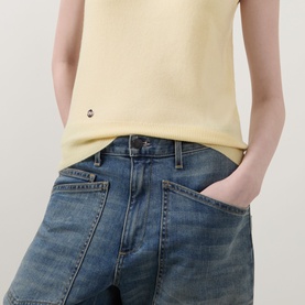 Model wearing Lucy Nagle The Crew Cashmere Top in Primrose yellow, sleeveless fine knit with logo disc detail, styled with mid-wash denim jeans