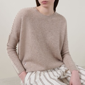 Model wearing Lucy Nagle The Stitch Cashmere Sweater in Light Weight Beige with stitch seam detailing, styled with white striped wide-leg trousers.