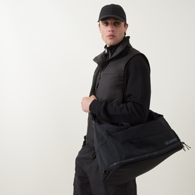 Model carrying Lululemon 3-in-1 Gym Duffle Bag in Black/Onyx Grey/Graphite Grey, styled with black gilet and cap.