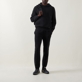 Model wearing Lululemon black hoodie with matching black joggers and dark trainers, hands in front pocket.