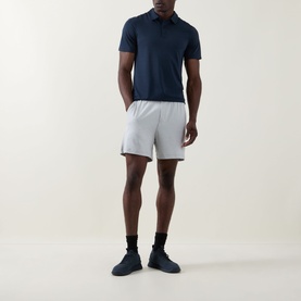 Model wearing Lululemon Reg Polo in True Navy, styled with light grey shorts and black socks with dark trainers.