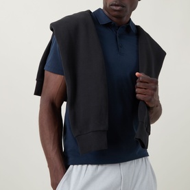 Model wearing Lululemon Reg Polo in True Navy, styled with a black sleeveless hoodie and white shorts.