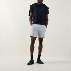 Model wearing Lululemon Reg Polo in True Navy, styled with a dark gilet, light grey shorts, black socks and navy trainers.
