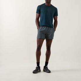 Model wearing Lululemon Pace Breaker Shorts 5" in Onyx Grey, styled with a teal t-shirt and black trainers.