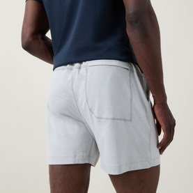 Model wearing Lululemon heathered silver drop shorts, rear view, styled with navy T-shirt, elasticated waistband and back patch pocket visible.