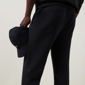 Model wearing Lululemon black sweatpants, styled with a matching black cap held in hand.