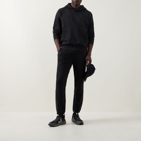 Model wearing Lululemon black sweatpants, styled with a matching black hoodie, cap, and dark trainers.
