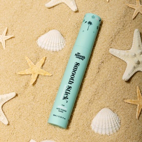 The Smooth Company Smooth Stick&trade; Island Edition teal tube styling stick, laid on sand surrounded by seashells and starfish.
