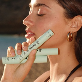 Model with The Smooth Company Smooth Stick&trade; Island Edition hair styling sticks in mint green packaging, gold hoop earrings visible