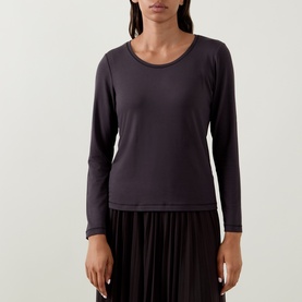 Model wearing Tuzzi Dark Chocolate long-sleeve scoop neck shirt in soft viscose blend, styled with a black pleated skirt.