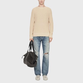 Model wearing All Saints ecru white cable-knit crew-neck jumper, styled with distressed light-wash jeans, carrying a black holdall bag.