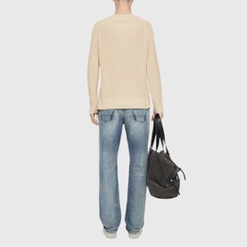 Model wearing All Saints ecru white knit jumper with light wash jeans, carrying a dark tote bag. Rear view.