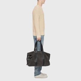 Model carrying a large dark brown leather tote bag with silver hardware and top handles, styled with a cream knit and light blue jeans.