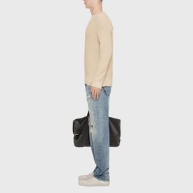 Model carrying a large black tote bag, styled with an All Saints ecru white knit jumper and light wash distressed jeans