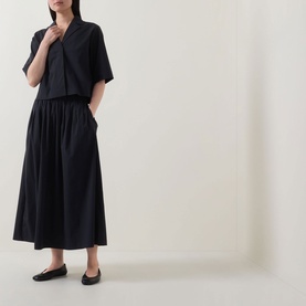 Model wearing Marc O Polo Woven Cropped Blouse in black with notch lapel, styled with a matching black maxi skirt and black ballet flats.