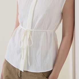Model wearing Marc O Polo Textured Waist-Tie Blouse in white, sleeveless with crinkle finish and tied waist detail, styled with tan trousers.