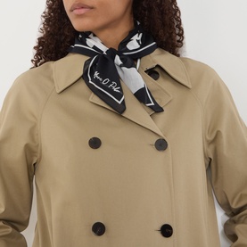 Model wearing a camel double-breasted trench coat with dark buttons, styled with a black and white printed neck scarf