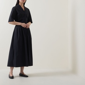 Model wearing Marc O Polo black midi skirt with elasticated waist and full silhouette, styled with a matching black wrap top and black ballet flats.