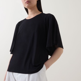 Model wearing Marc O Polo black oversized T-shirt with wide sleeves and crew neck, styled with white wide-leg trousers