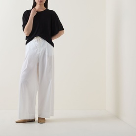 Model wearing Marc O Polo black short-sleeve relaxed T-shirt, styled with wide-leg white trousers and beige flats.