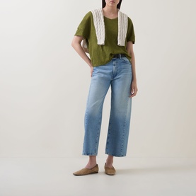 Model wearing Marc O Polo Wide Slub T-Shirt in Shaded Fern with light-wash wide-leg jeans, cream knit vest and tan mules.