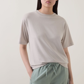Model wearing Marc O Polo Solid Relaxed T-Shirt in Linen Beige, relaxed fit, round neck, short sleeves, styled with sage green drawstring trousers.