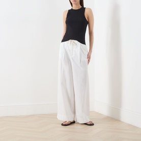 Model wearing Marc O Polo black sleeveless modal cotton T-shirt with white wide-leg trousers and dark flat sandals.