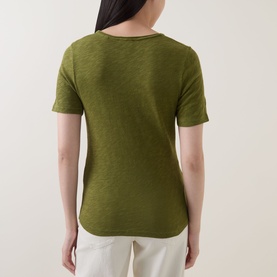 Model wearing Marc O Polo Solid Slub T-Shirt in Shaded Fern, scoop neck, short sleeves, curved hem, back view, styled with white trousers.