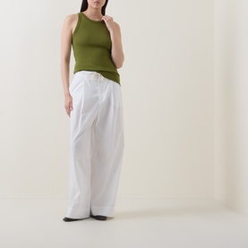 Model wearing Marc O Polo Solid Logo Tank Top in Shaded Fern, styled with wide-leg white trousers and black flat shoes.
