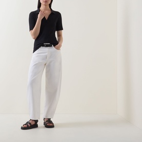 Model wearing Marc O Polo Pointelle Polo Sweater in black with V-neck collar, styled with white wide-leg trousers and black sandals.