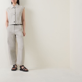Model wearing Marc O Polo Linen Beige trousers, styled with a sleeveless collared top, belt, and black chunky sandals.