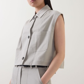 Model wearing Marc O Polo Linen Beige sleeveless cropped shirt vest with button front and chest pocket, styled with matching trousers and belt.