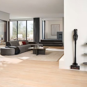 Miele Triflex HX3 Aqua cordless vacuum cleaner in black, mounted on wall charging dock in bright modern living room with wooden floors.