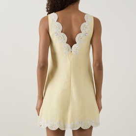 Model wearing Jonathan Simkhai Edena Embroidered Linen Mini Dress in Buttercream, rear view showing scalloped trim and embroidered detailing.