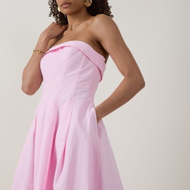 Model wearing Jonathan Simkhai Avril Bustier Dress in Daisy pink, strapless with folded bodice detail and pleated skirt, styled with gold earrings