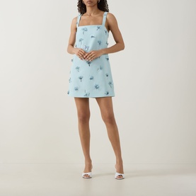 Model wearing Jonathan Simkhai Ella Embellished Mini Dress in blue with floral embellishment and square neckline, styled with white heeled mules