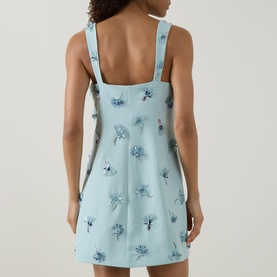 Model wearing Jonathan Simkhai Ella Embellished Mini Dress in blue, rear view showing floral embellishment, fixed straps and square neckline