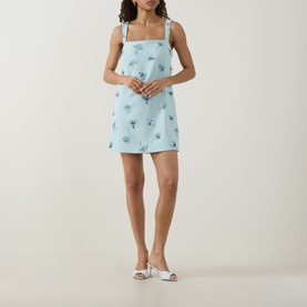 Model wearing Jonathan Simkhai Ella Embellished Mini Dress in blue with floral detail and square neckline, styled with white heeled mules